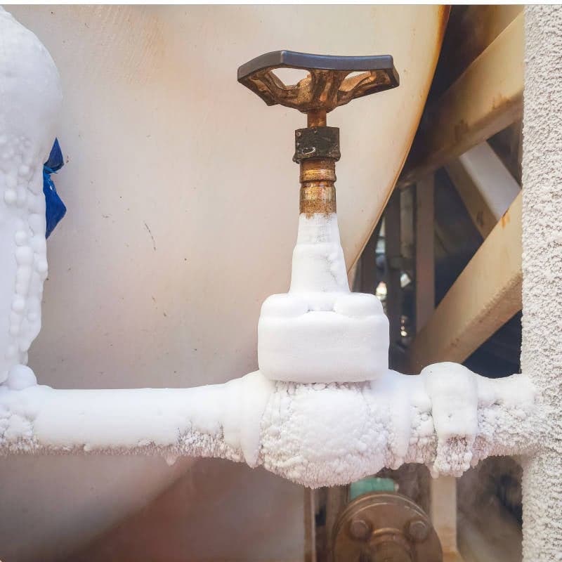 A metal valve and pipe covered in frost and ice, indicating exposure to extremely cold temperatures or handling of cryogenic substances, often seen before line thawing operations.