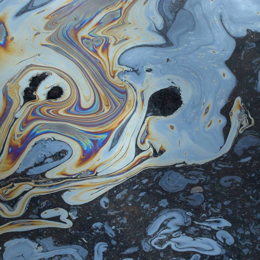 Oil slick on water surface creating swirling iridescent patterns with dark patches showing through, highlighting the importance of regular oil separator cleaning.